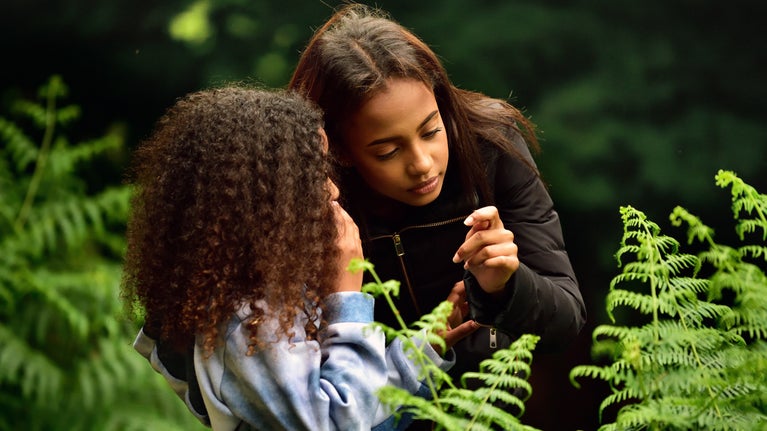 Two girls looking at a fern while standing among tall plants